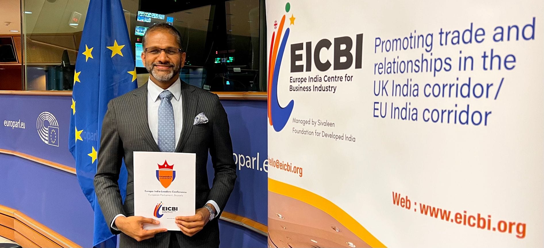 Rahul Venkit holding an EICBI folder in front of European Parliament flags